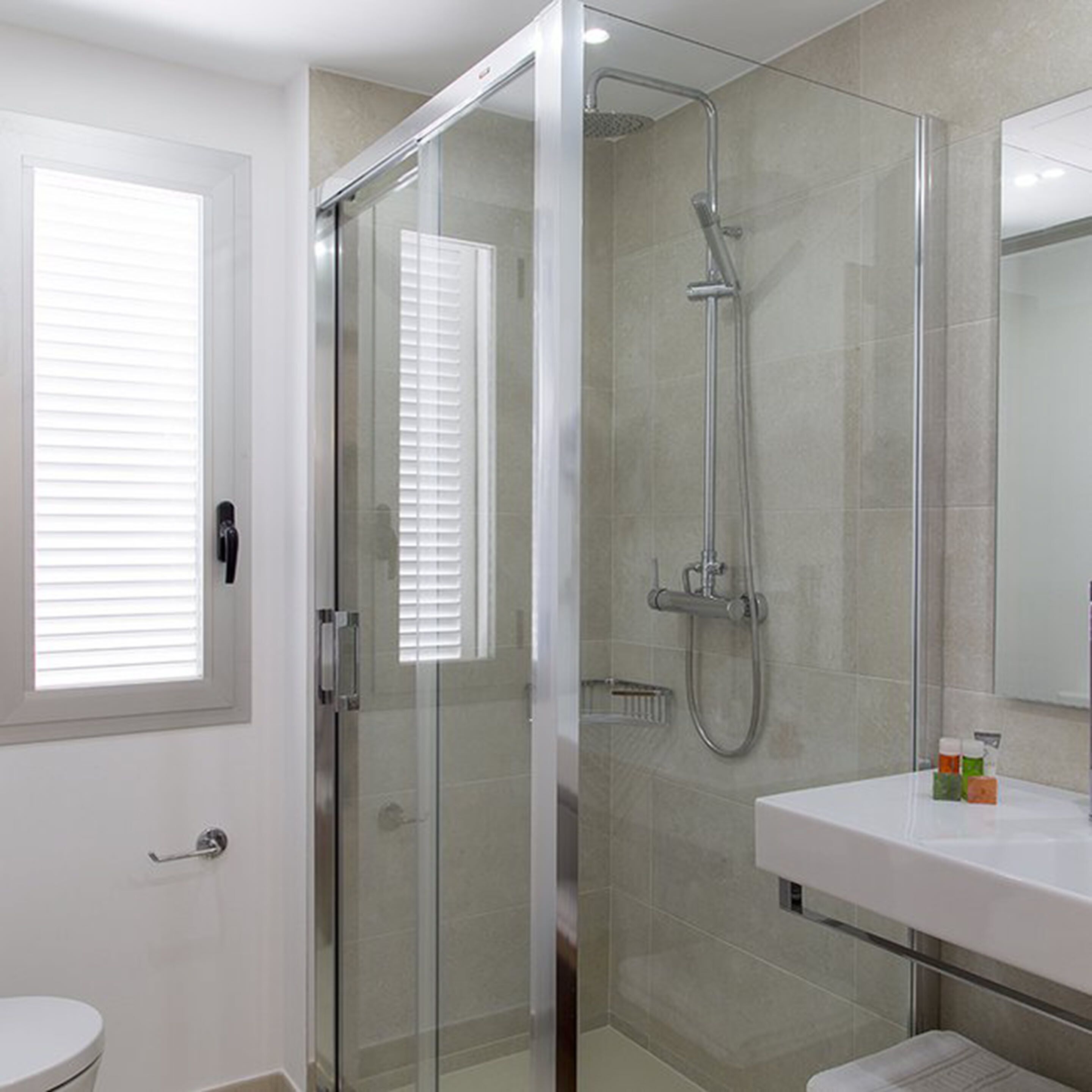A modern bathroom with a glass-enclosed shower, a white sink, and a toilet.