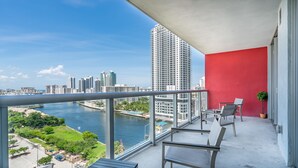 A balcony with a city view, a red wall, and a small table with chairs. - Resort Apartments (Hallandale Beach)