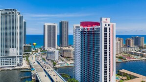 A high-rise hotel with a prominent red and white facade, located near a waterfront with a bridge and road. - Resort Apartments (Hallandale Beach)