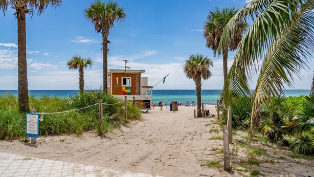 A beach with a lifeguard tower, palm trees, and a clear blue sky. - Resort Apartments (Hallandale Beach)