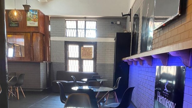Een modern interieur met een glazen tafel, omringd door stoelen, een met baksteen beklede muur met een Hennessy bord en een raam met roedeijzer.