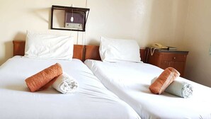 Een hotelkamer met twee bedden, elk voorzien van witte lakens en opgerolde handdoeken. Een radio is aan de muur boven de bedden bevestigd.