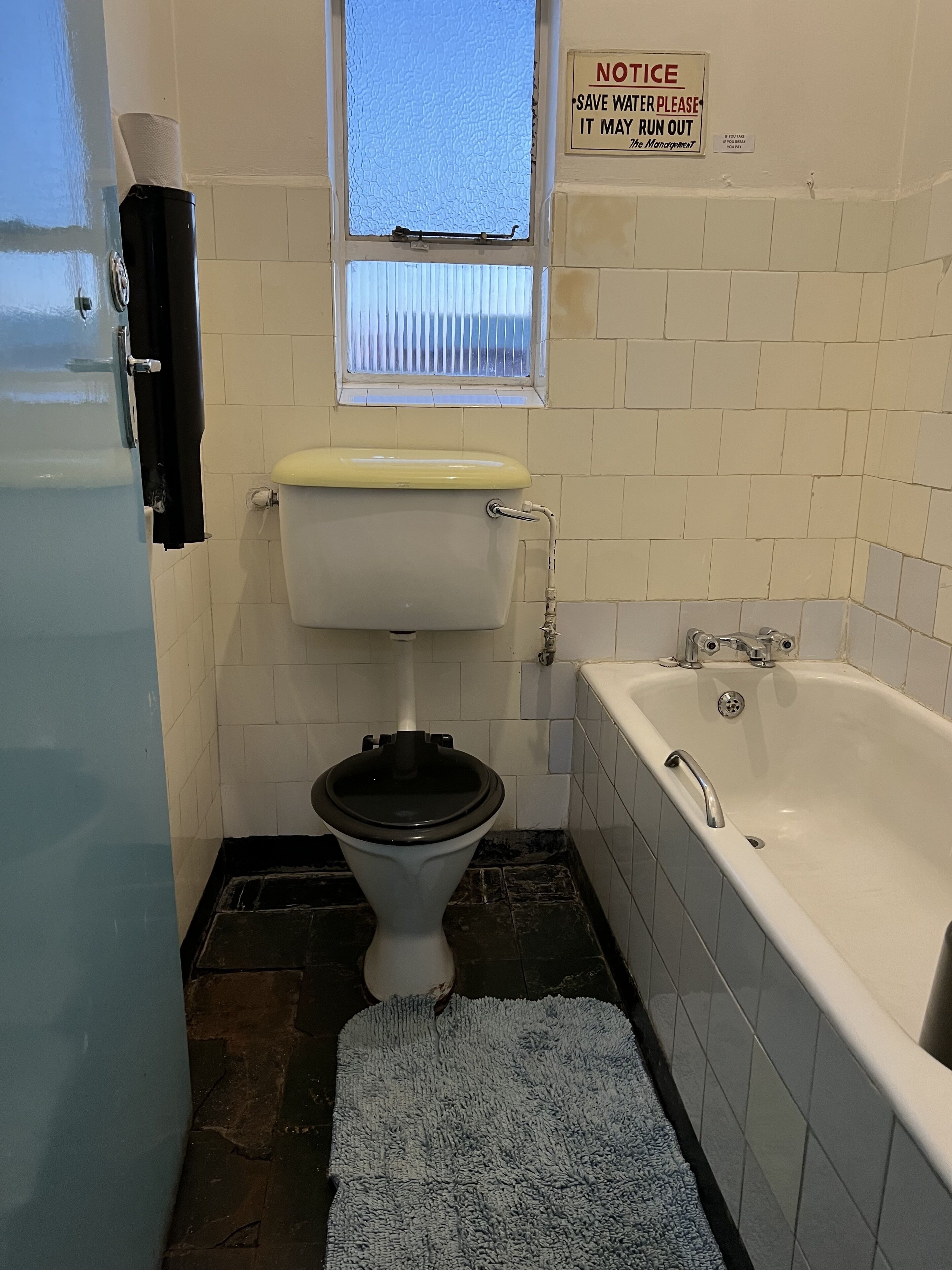 A small bathroom with a toilet, a window, a bathtub, and a notice sign.