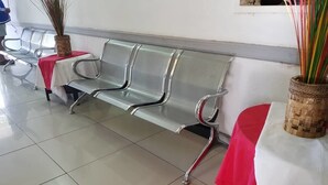 Een rij metalen stoelen met een rode tafelkleed, een gevlochten mand met een plant, en een betegelde vloer.