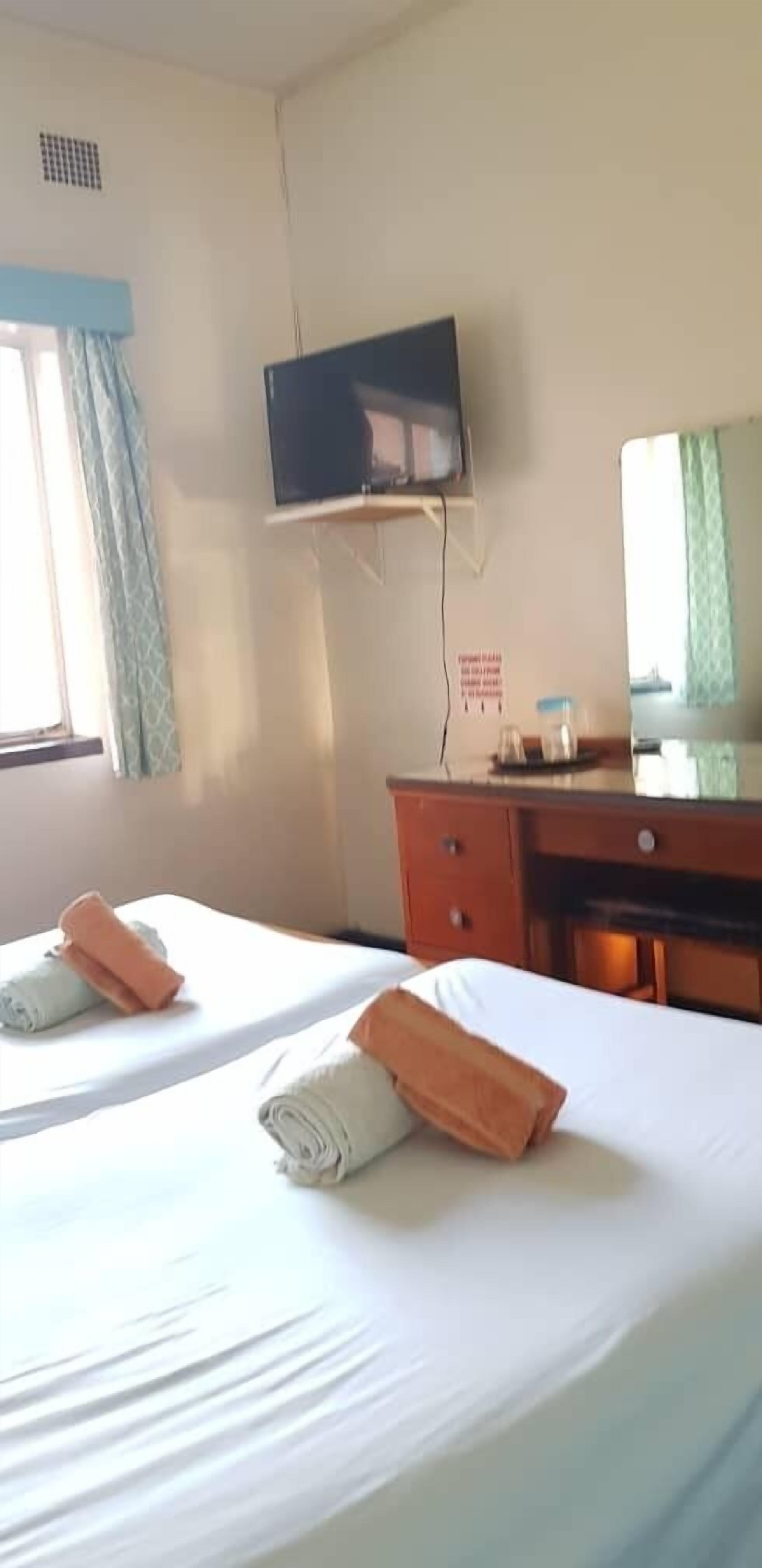 A hotel room with two beds, a TV mounted on the wall, a desk with a mirror, and a window with curtains.