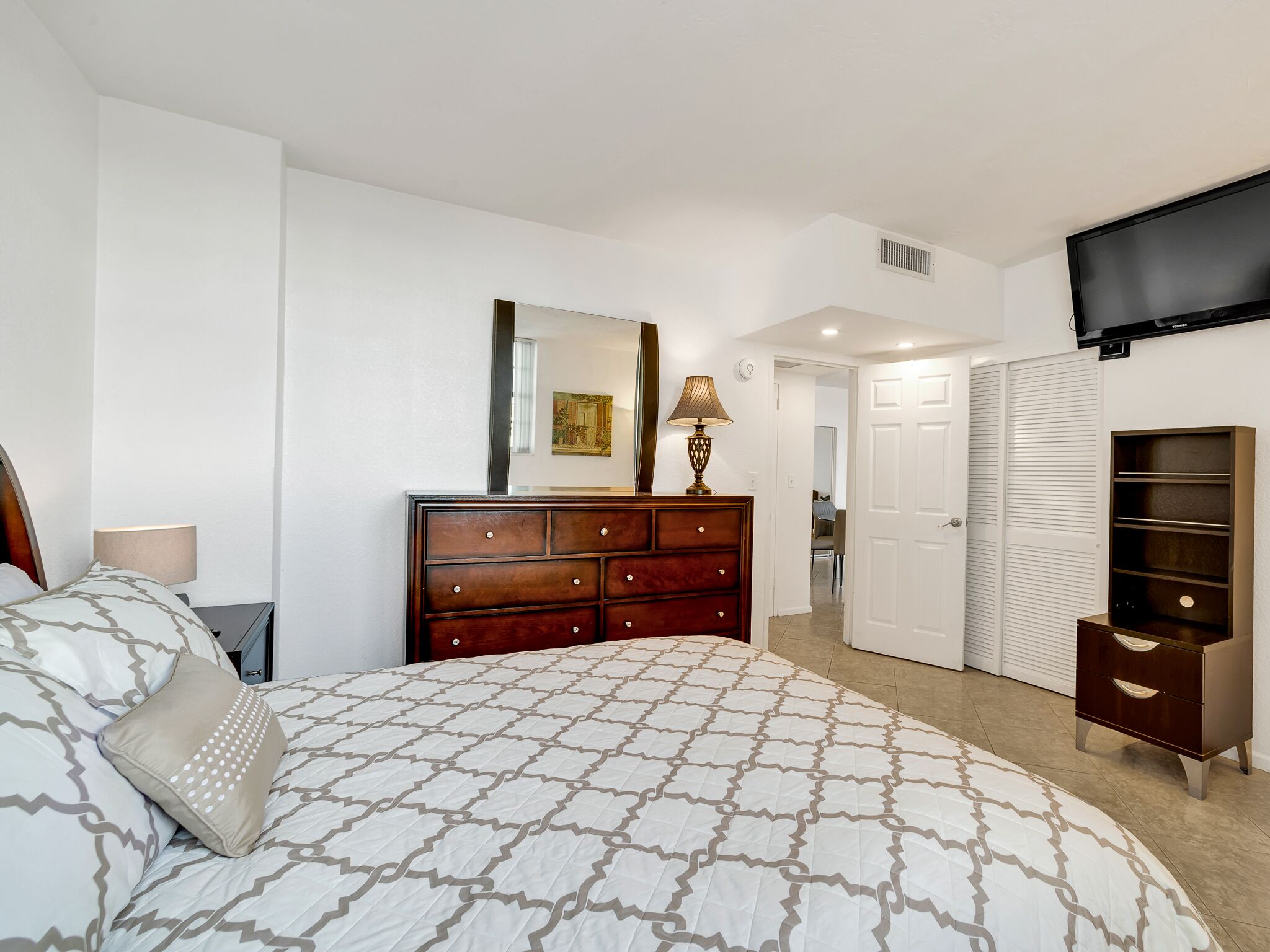 A bedroom with a bed, dresser, wardrobe, and a television.