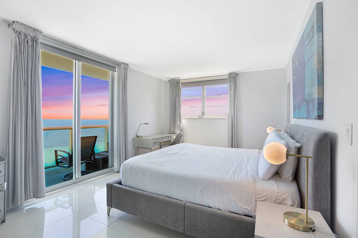 A modern hotel room with a large bed, a desk, and a view of the ocean.