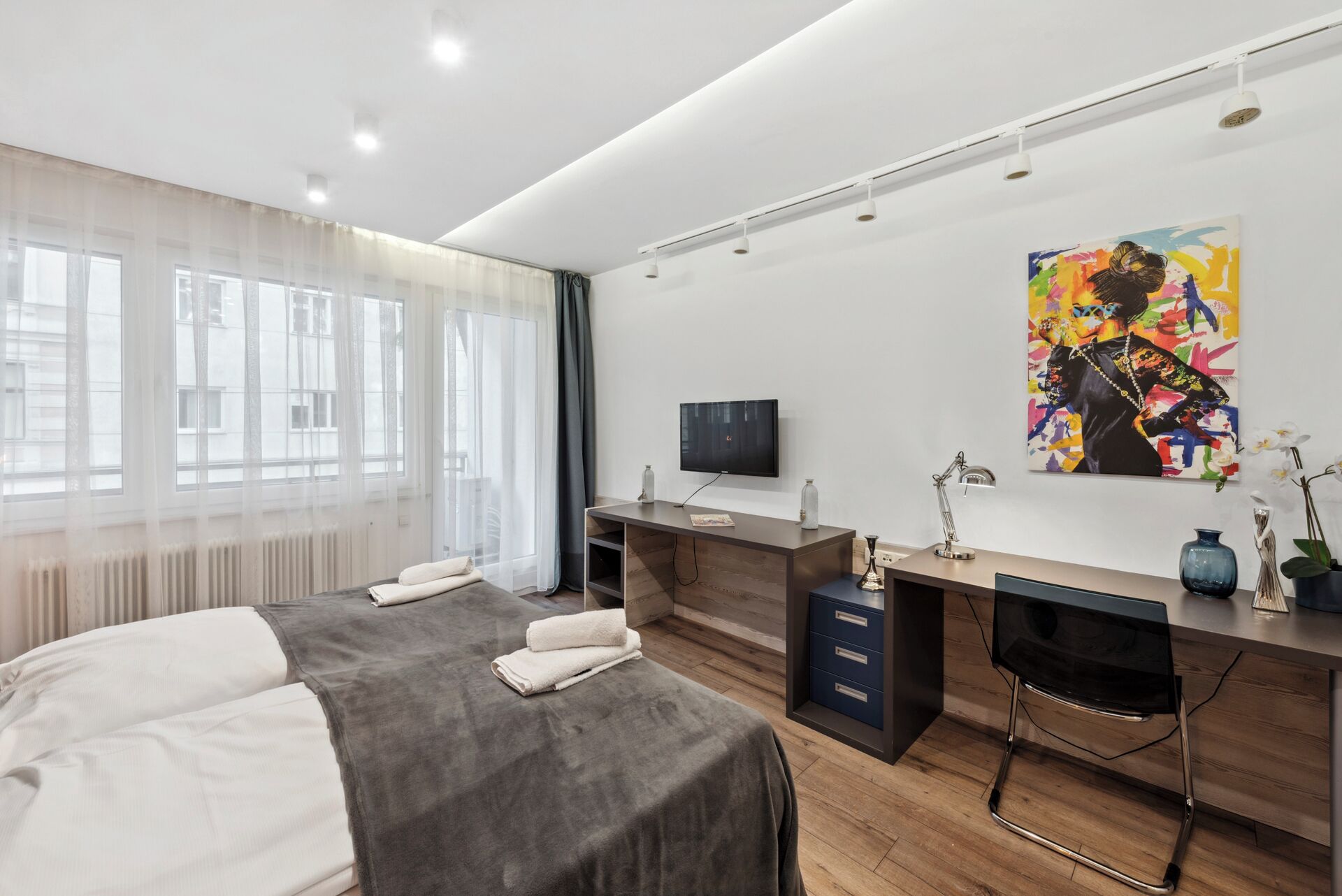 Una habitación de hotel moderna con dos camas, un escritorio, un televisor y un cuadro de colores en la pared.