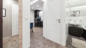 Ein modernes Hotelzimmer mit einem großen Bett, einem Nachttisch und einem Kleiderschrank. Es gibt ein Badezimmer mit Waschbecken und Spiegel.