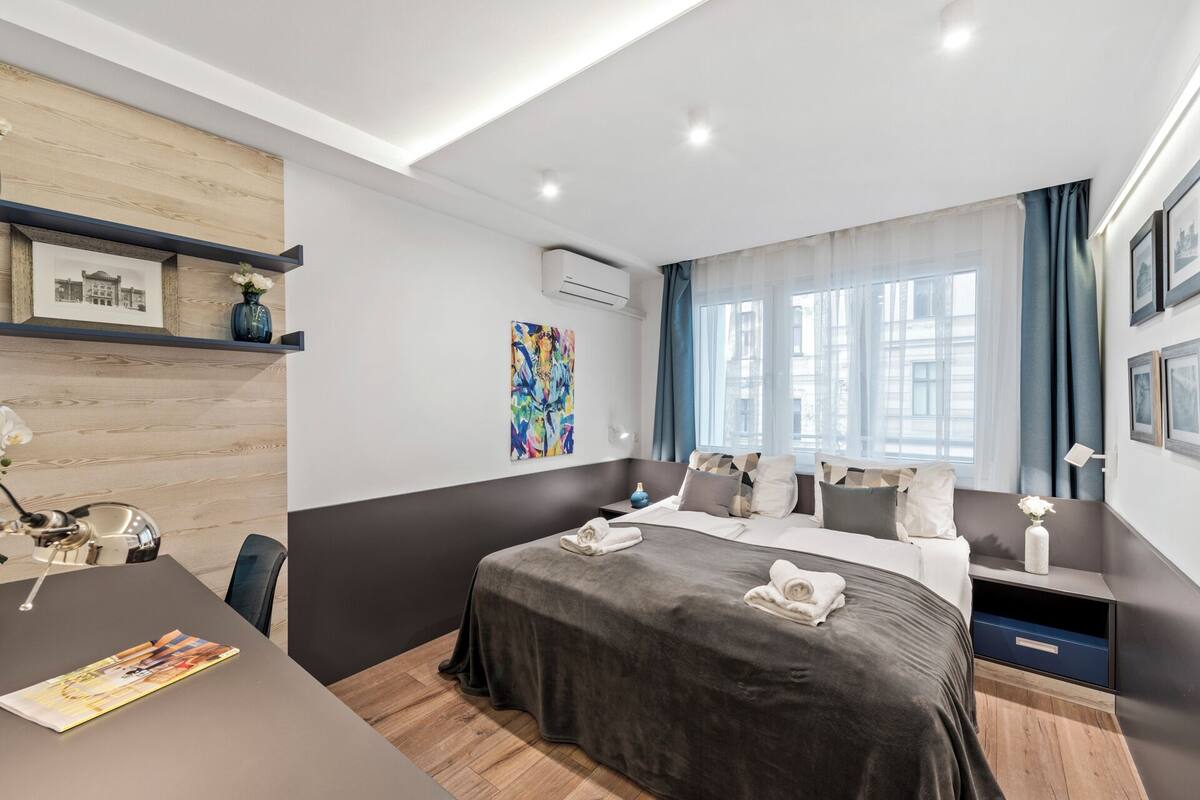 A modern hotel room with a large bed, a desk, and a window with curtains.