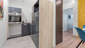 Eine moderne Küche mit Edelstahlgeräten, einer Wand in Holzoptik und einem Essbereich mit einem blauen Stuhl.