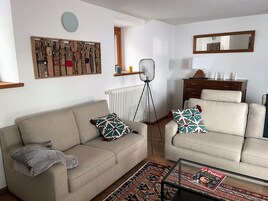 A living room with a sofa, armchair, and coffee table. There is a radiator, a floor lamp, and a mirror on the wall.