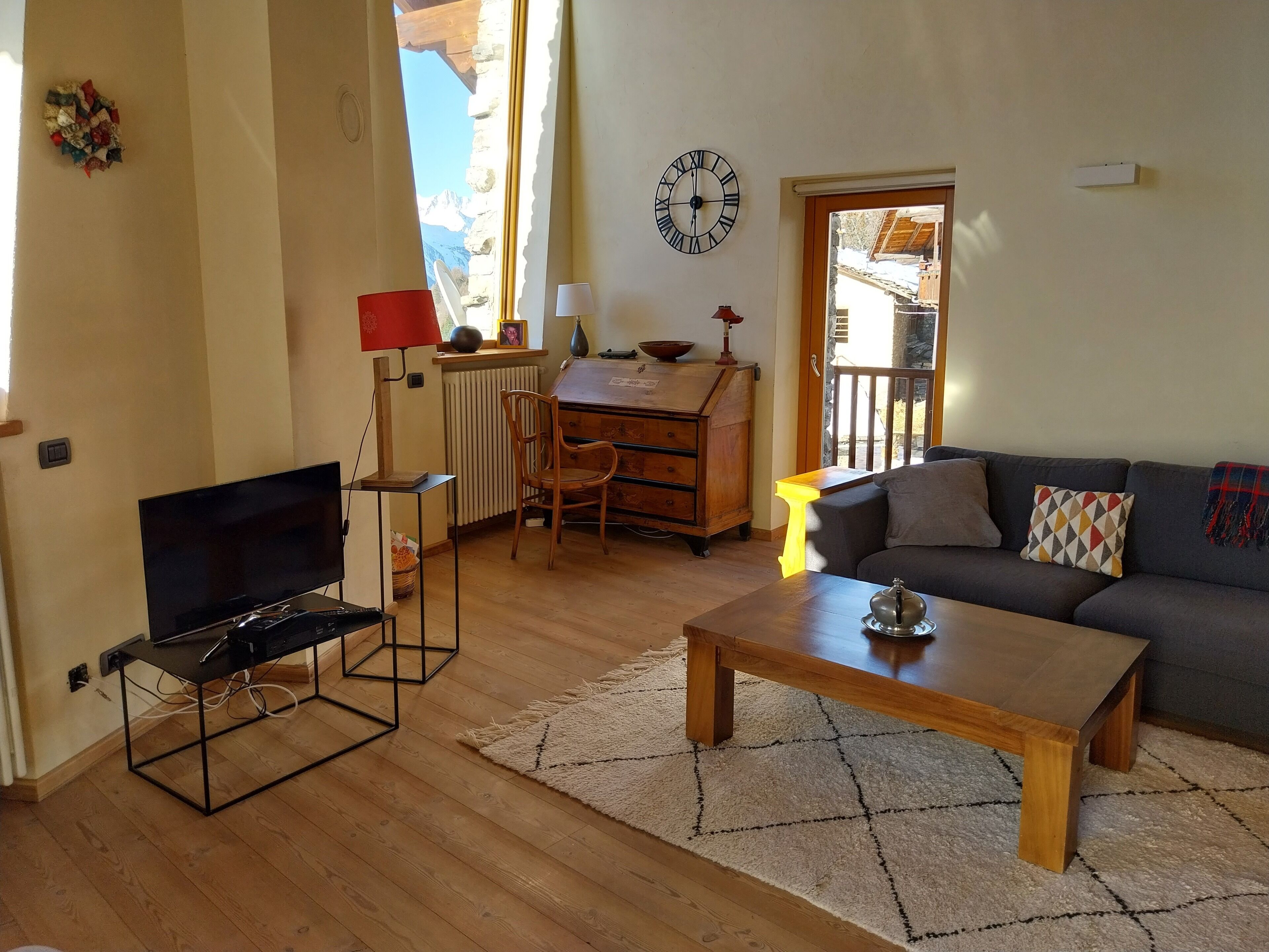 A living room with a TV, wooden coffee table, sofa, and a view of mountains through a window.