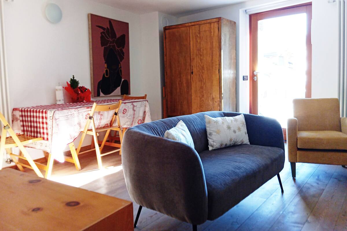 A living room with a blue sofa, a wooden cabinet, a dining table with a red and white checkered tablecloth, and a painting on the wall.