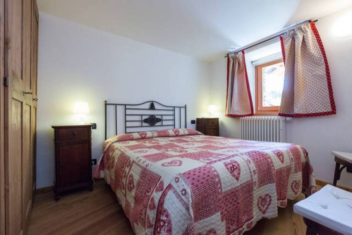 A bedroom with a bed, bedside tables, a window with curtains, and a radiator.