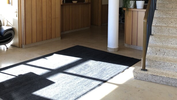 Un interior espacioso con paneles de madera, una alfombra negra, una escalera y un reloj en la pared.
