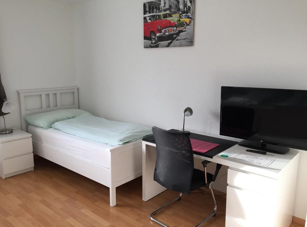 A bedroom with a bed, a desk with a chair, a TV, and a nightstand.