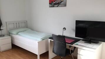A bedroom with a bed, a desk with a chair, a TV, and a nightstand.