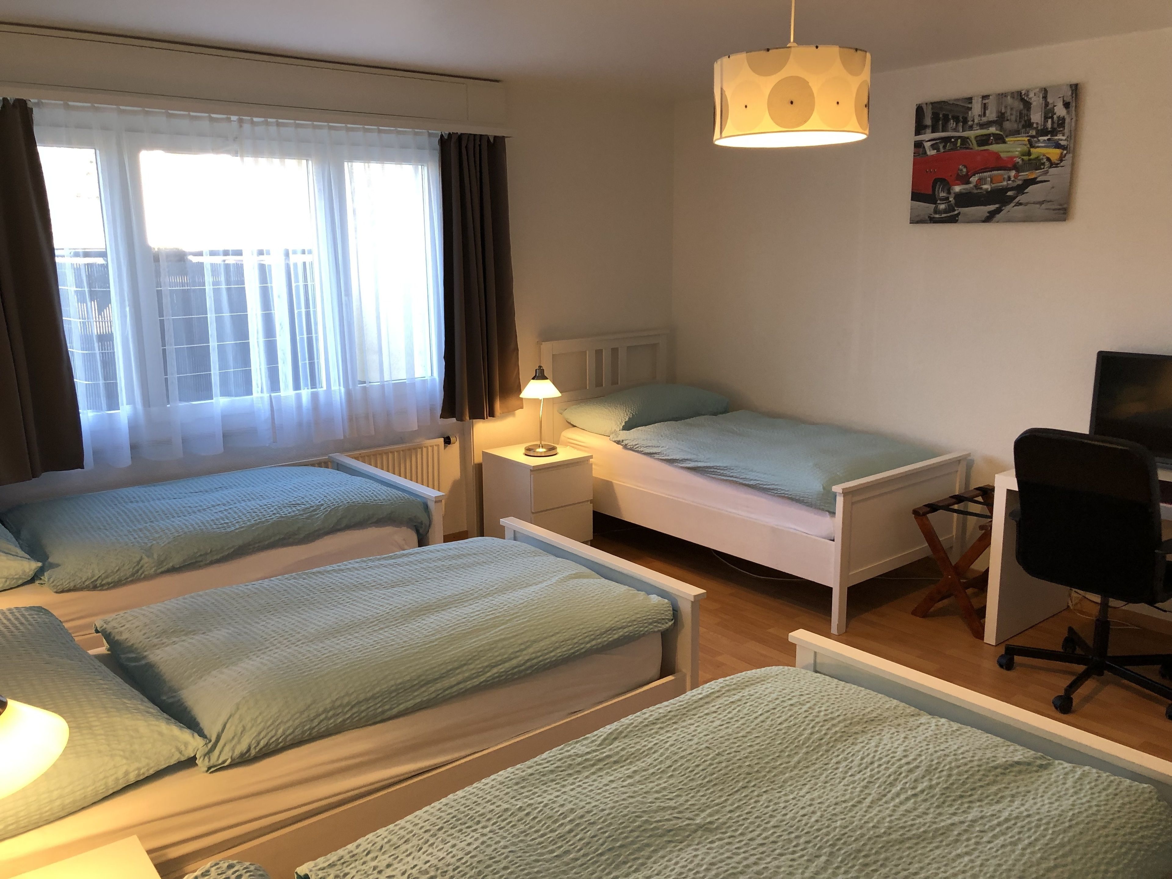 Une chambre d’hôtel avec deux lits simples, un bureau avec une chaise, un radiateur et une fenêtre avec des rideaux.