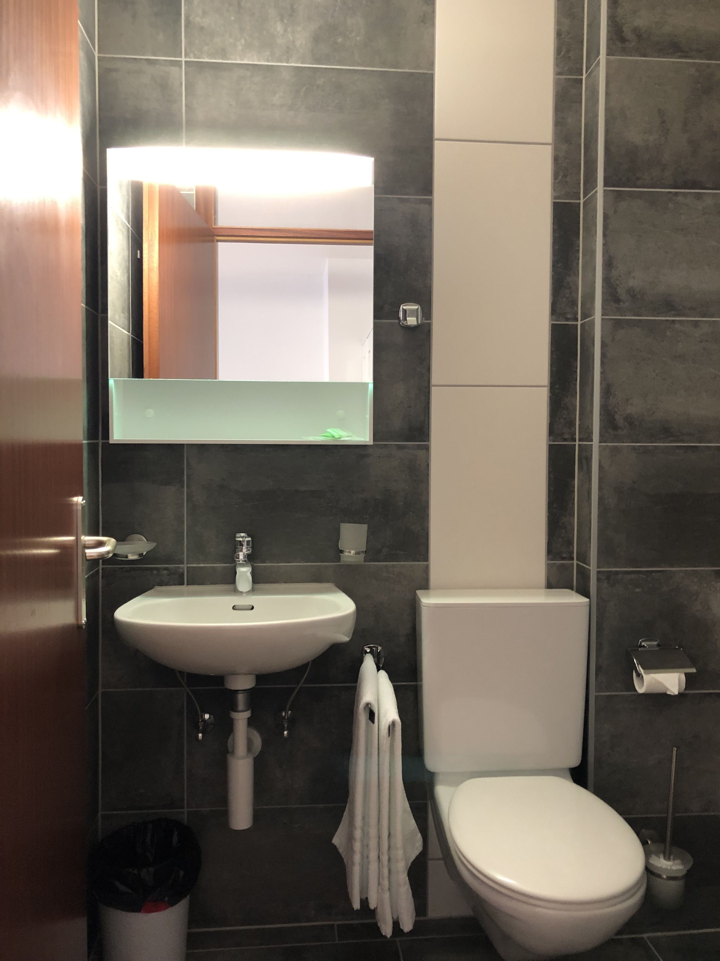 A modern bathroom with a white sink, toilet, and a mirror above the sink.