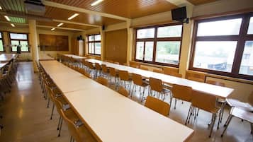 Un salón de conferencias con largas mesas y sillas, ventanas amplias y paneles de madera en el techo.