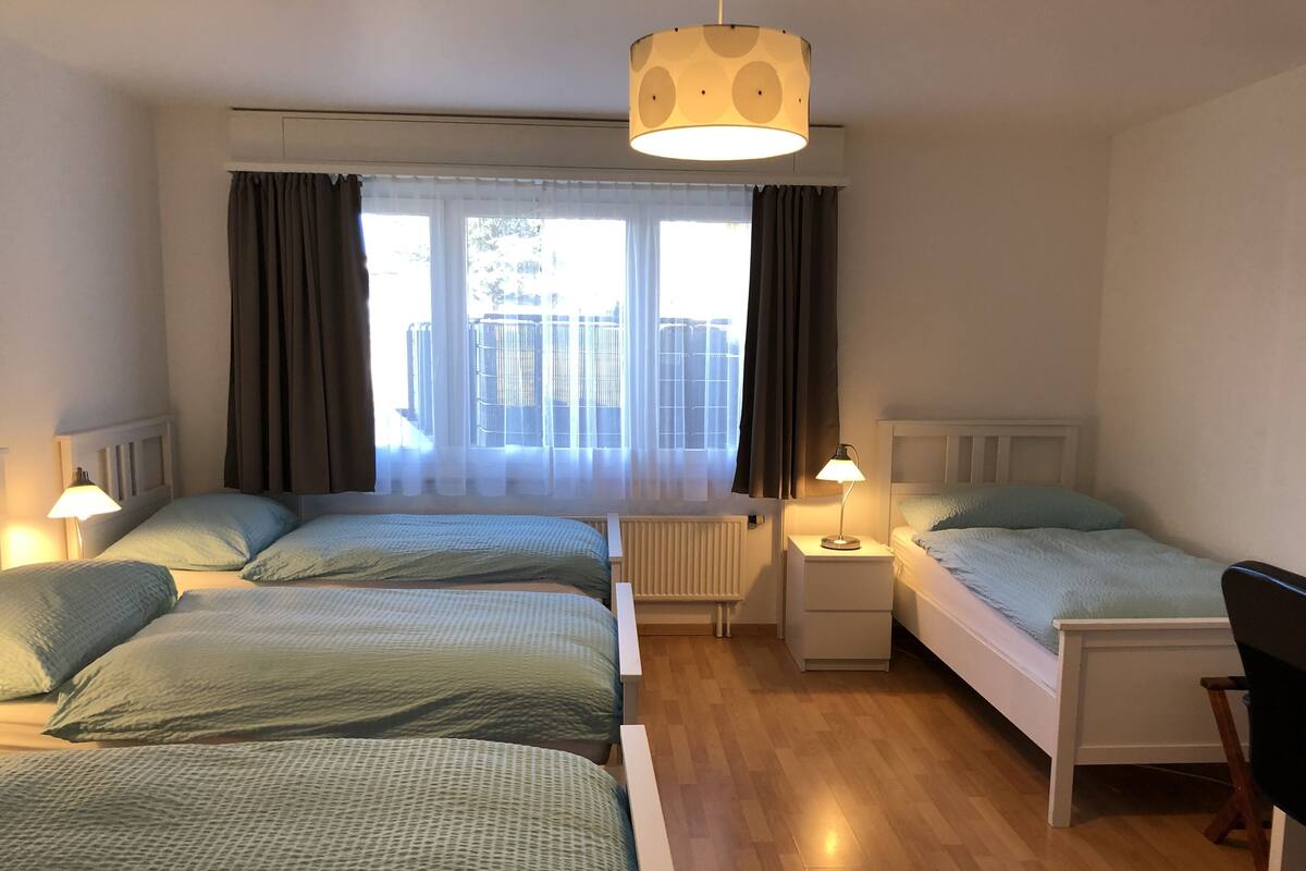 A hotel room with two beds, a desk, a chair, and a window with curtains.
