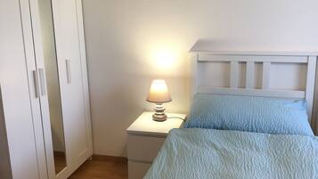 Un dormitorio con una cama, una mesita de noche con lámpara, un armario y dos cuadros colgados en la pared.