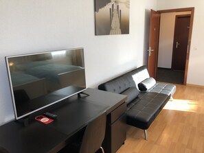 Una habitación moderna con cama, escritorio con computadora, sofá y puerta que da a otra habitación.