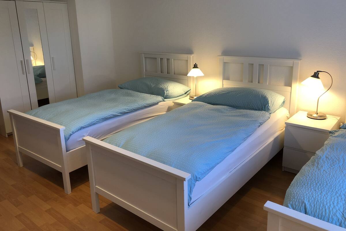 A bedroom with two single beds, each with a bedside table and lamp, and a wardrobe.