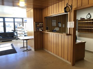 Un área de recepción con paneles de madera, un mostrador de recepción, un reloj, un calendario y una ventana con vistas al exterior.