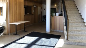Un vestíbulo de hotel con paneles de madera, un mostrador de recepción, un reloj, una escalera y una planta en maceta.