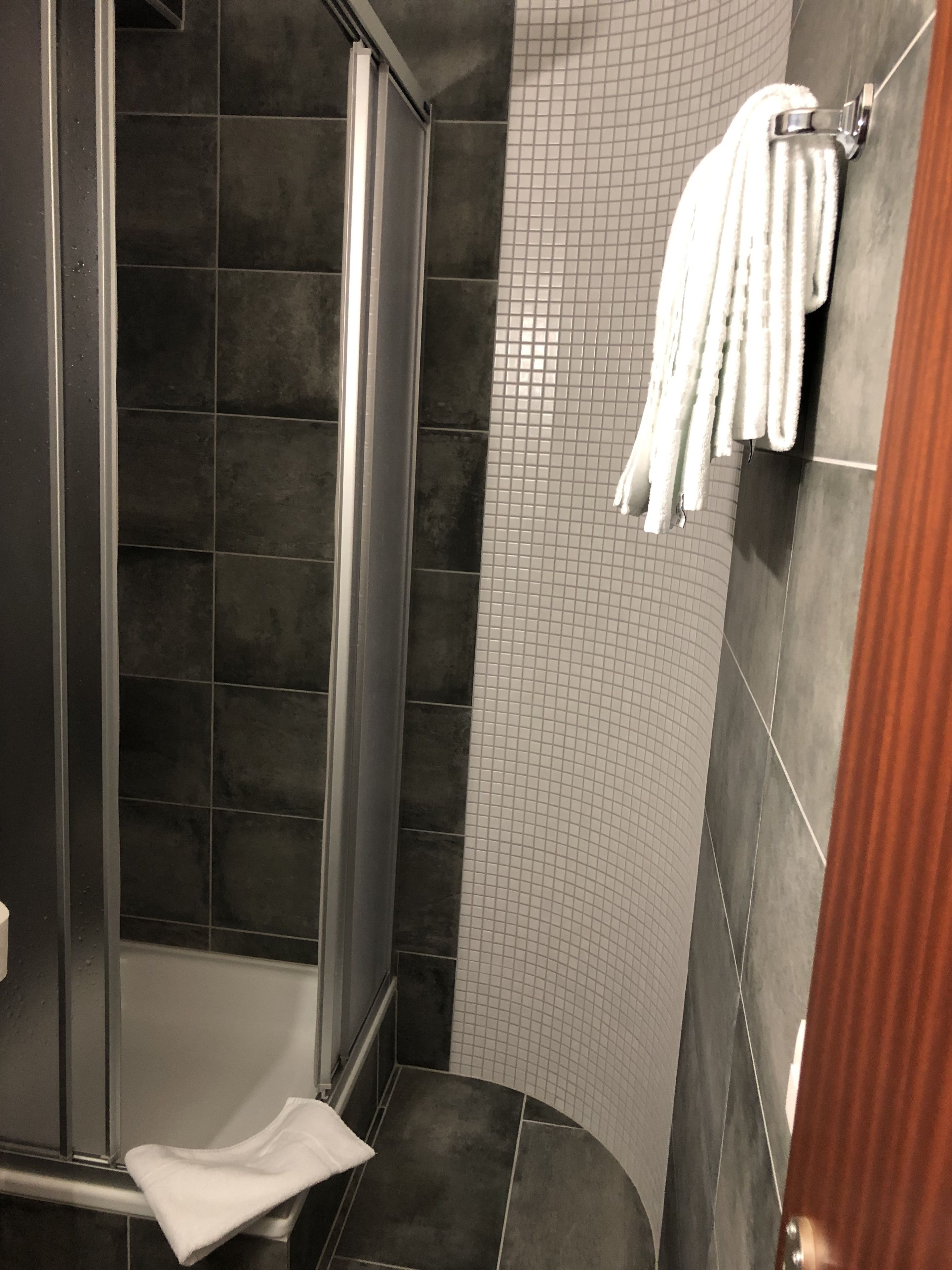 Une salle de bain avec des carreaux de couleur foncée, un espace douche et un porte-serviettes avec des serviettes.