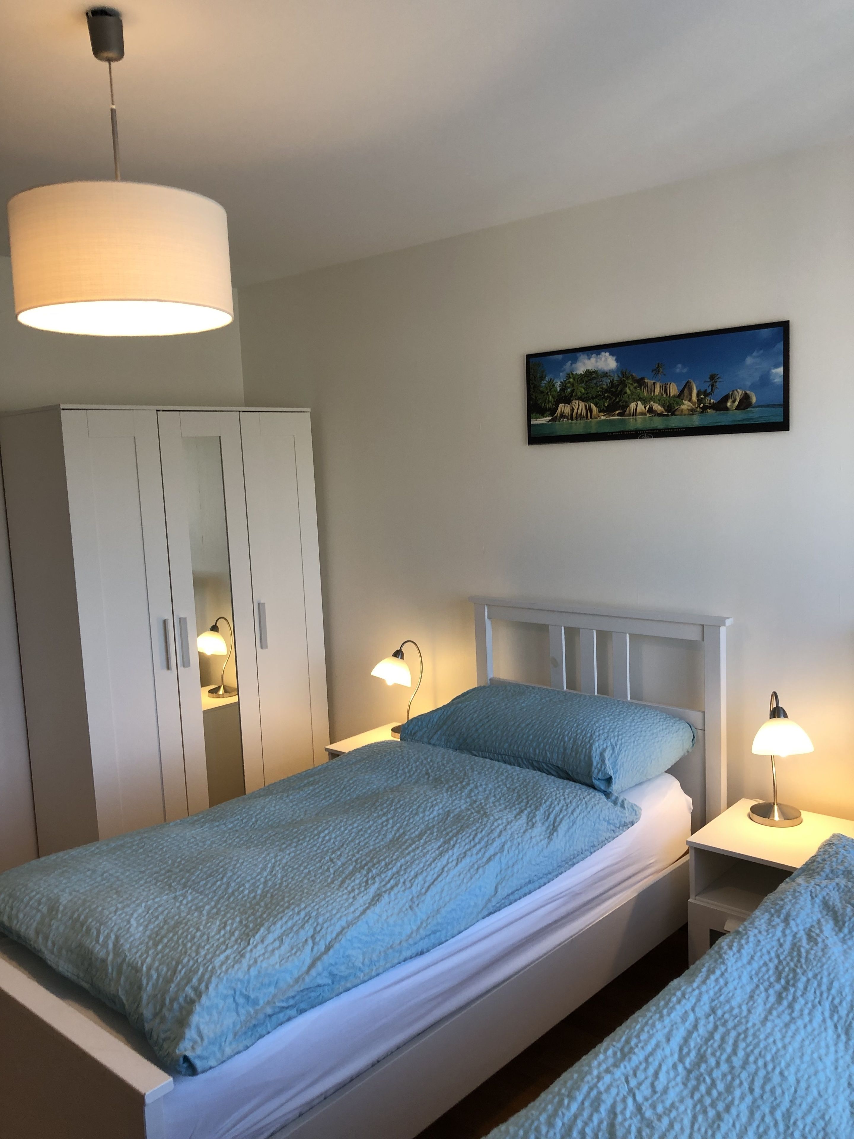 A bedroom with a bed, bedside lamps, a wardrobe, and a painting on the wall.