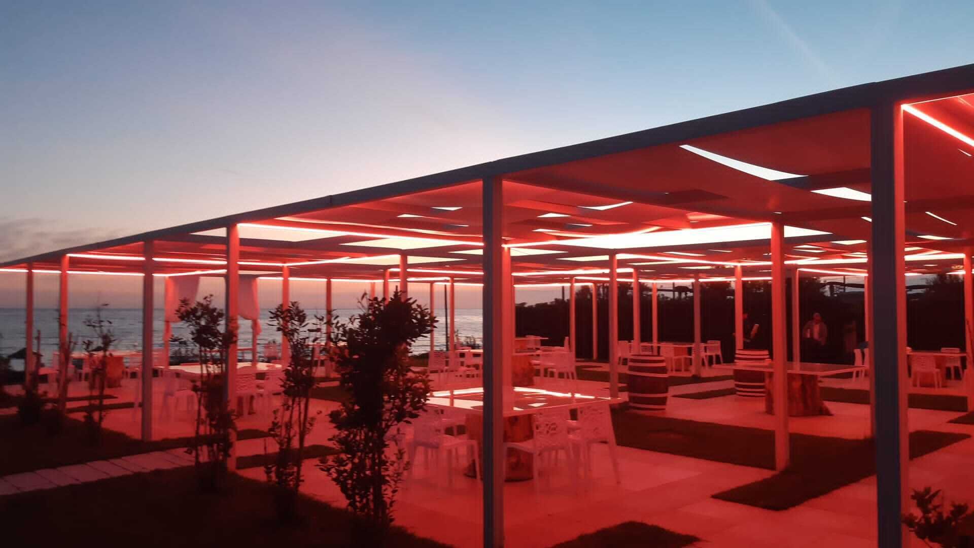 An outdoor seating area with a view of the sea, covered by a transparent roof structure.