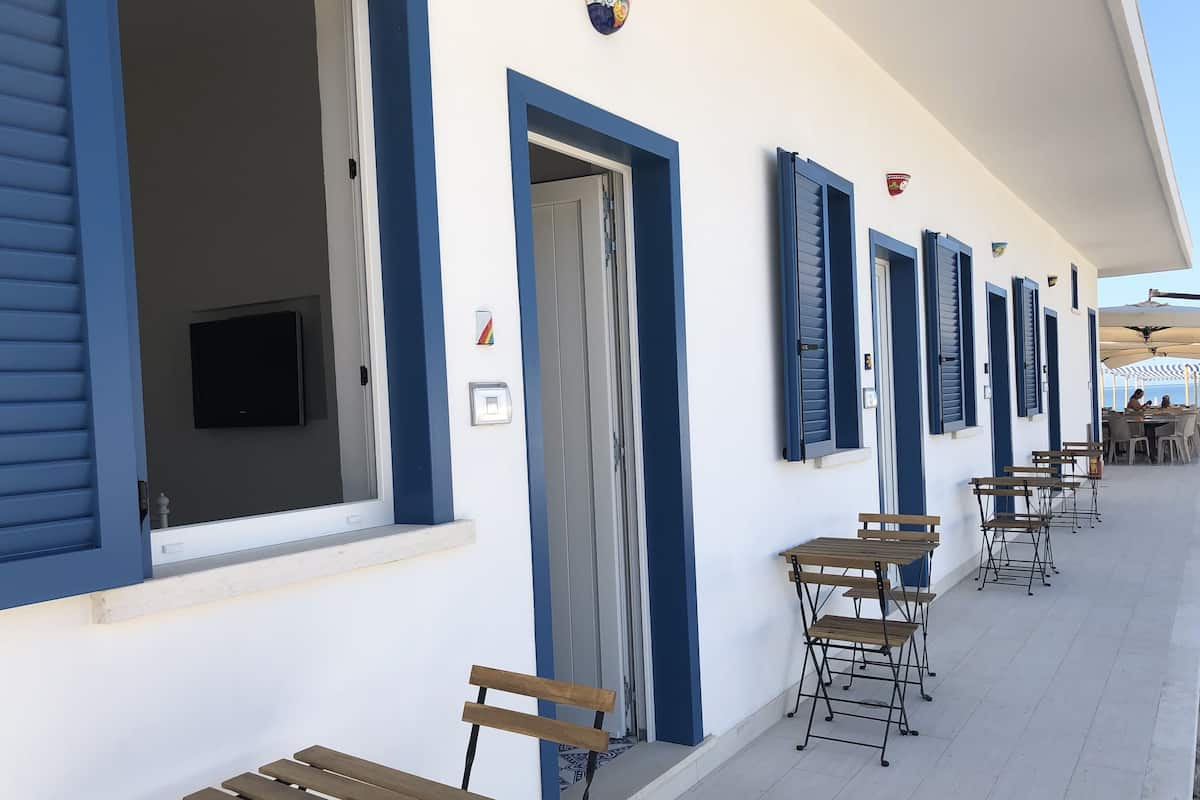 A building with blue-framed windows and doors, outdoor seating with benches and tables, and a tiled floor.