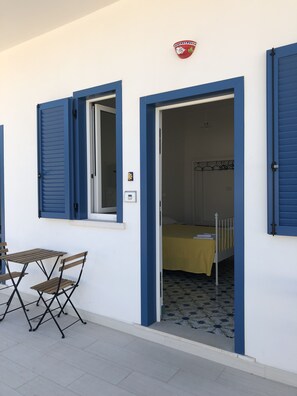 Una habitación con una cama, una pequeña mesa con sillas y una ventana con contraventanas azules.