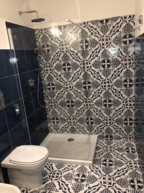 Un baño con ducha, inodoro y azulejos estampados.