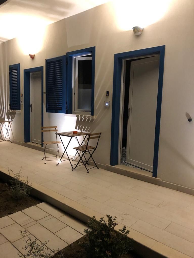 Un pasillo con puertas cerradas, una pequeña mesa con sillas y una botella de agua en el suelo.