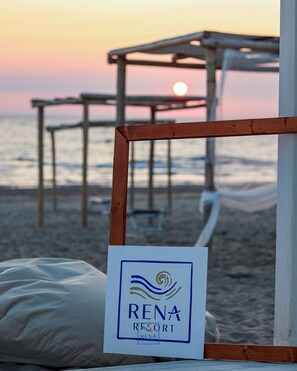 Vista de la playa con una estructura de madera y un letrero del Resort Rena.