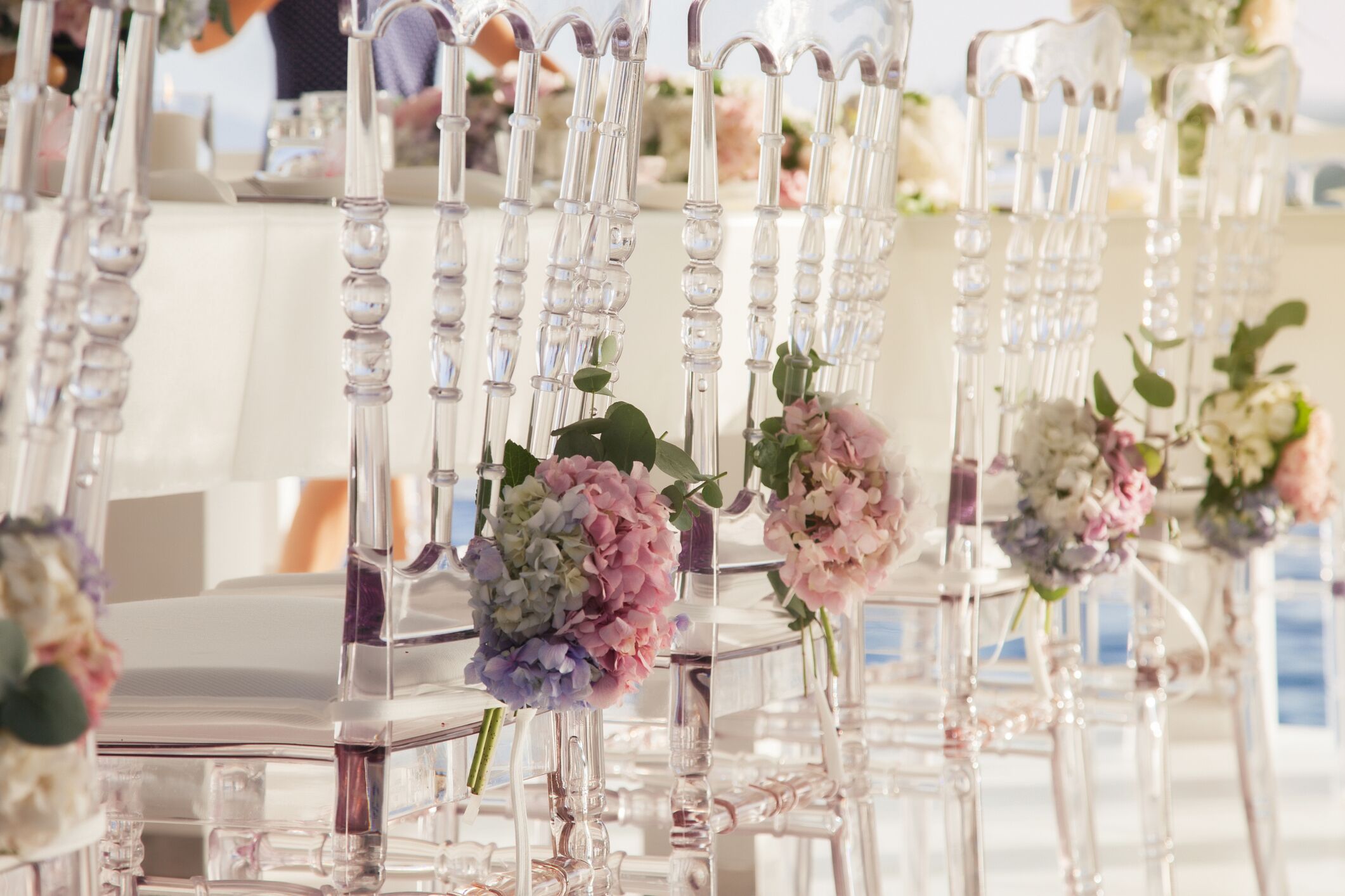 Rows of clear chairs with floral centerpieces, arranged in a formal setting.