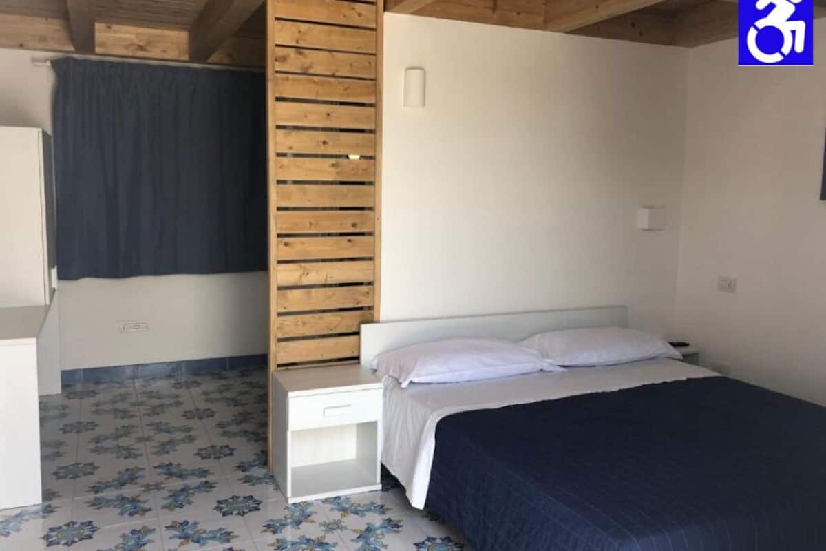 A bedroom with a bed, a wooden slat wall, a white nightstand, and a blue patterned floor.