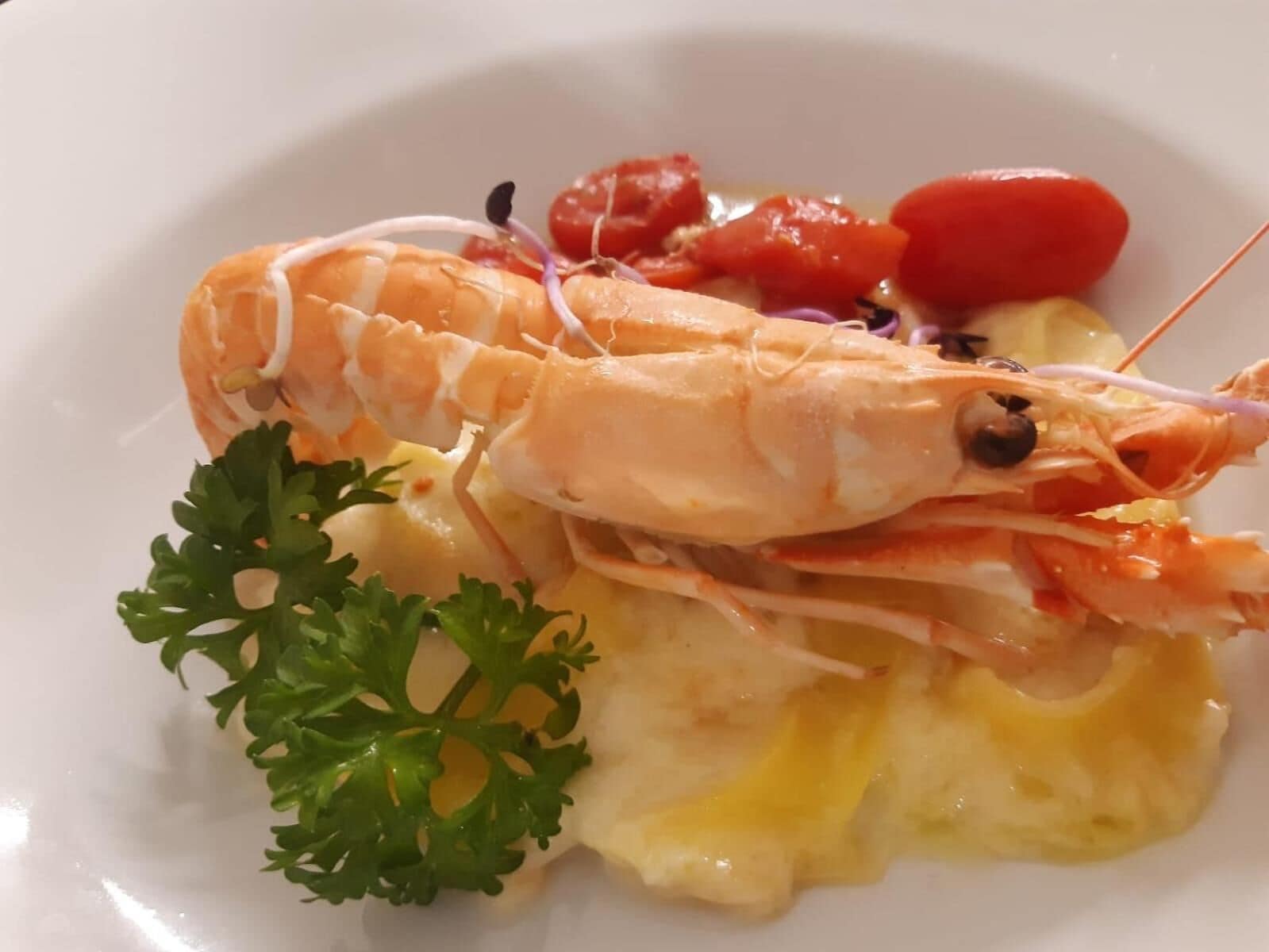 A plate with a cooked shrimp, red tomatoes, and a garnish of parsley.