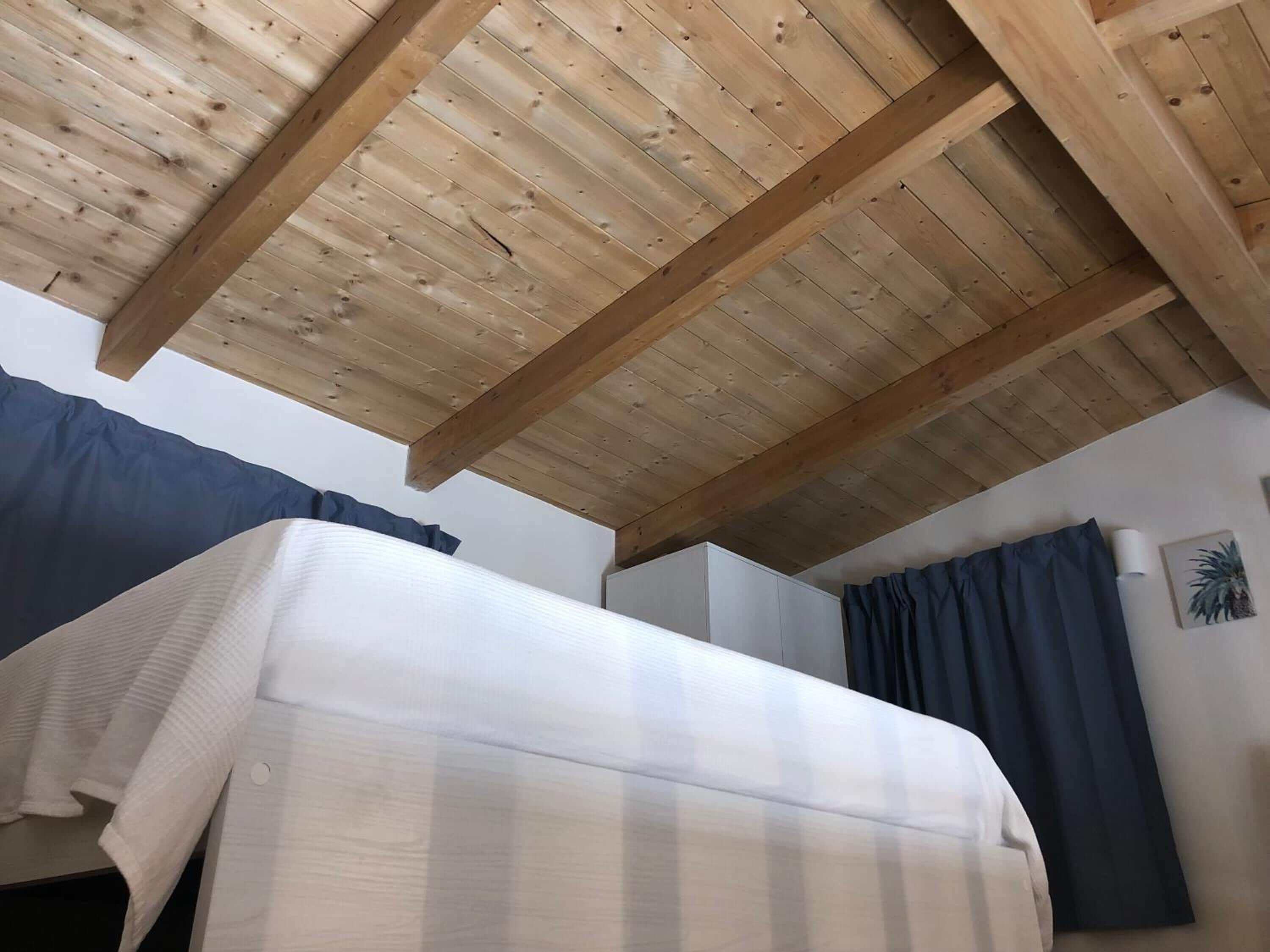 Une pièce avec un plafond en bois, un lit avec un matelas blanc et un rideau bleu.