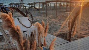 A beachside wedding setup with a wooden deck, pampas grass decorations, and a sunset view. - Rena Resort (Mondragone)