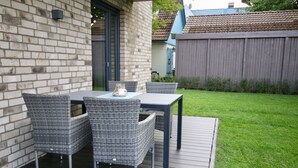 An outdoor patio with a table and four wicker chairs, a small decorative vase, and a wooden deck. - Kapitänshaus 1 (Kellenhusen)