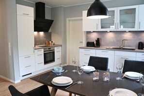 A modern kitchen with white cabinets, a black countertop, and a dining table set for four. - Kapitänshaus 1 (Kellenhusen)