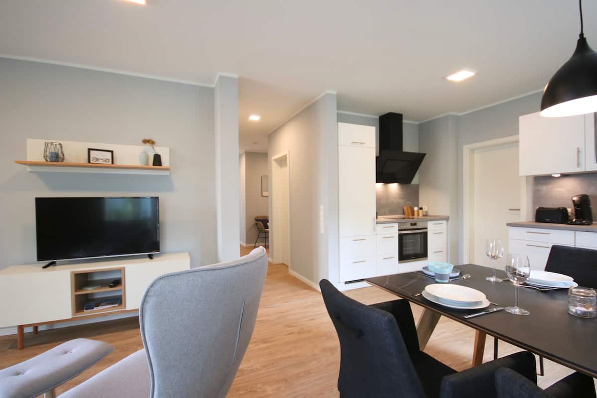 A modern kitchen with white cabinets, a black range hood, and a dining area with a table set for two.