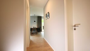 A hallway with a wooden floor leading to a dining area with a table and chairs. - Kapitänshaus 1 (Kellenhusen)