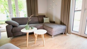 A modern living room with a grey sectional sofa, a small round table, and a vase with a plant. - Kapitänshaus 1 (Kellenhusen)