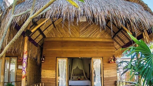A thatched-roof bungalow with a wooden exterior, a balcony with a wooden bench, and a bed with a canopy. - Pondok Kana Homestay (Penida Island)